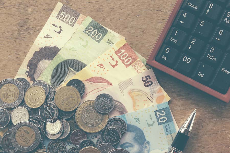 Varios billetes y monedas de pesos mexicanos frente a una calculadora.