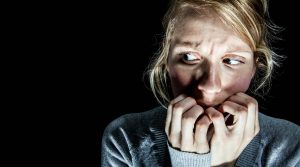 Percepción de riesgo, mujer rubia asustada comiéndose las uñas sobre fondo negro